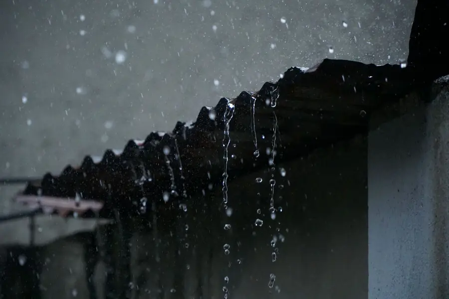 Rainwater dripping off the edge of a roof in heavy rain, the leak that comes back after a poor repair by an unchecked roofer