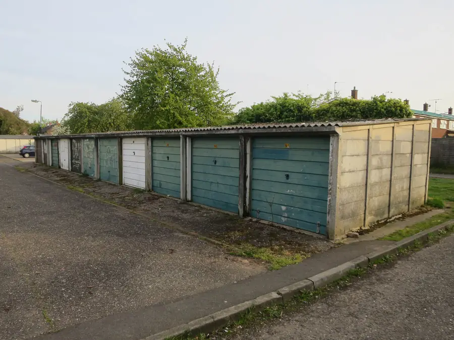 Run of prefabricated concrete garages with weathered corrugated cement sheet roofs and moss along the eaves