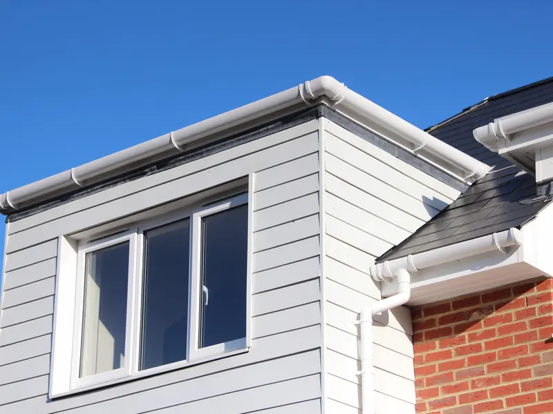 Clad dormer window with new white uPVC fascia boards, round guttering and a downpipe running past red brickwork