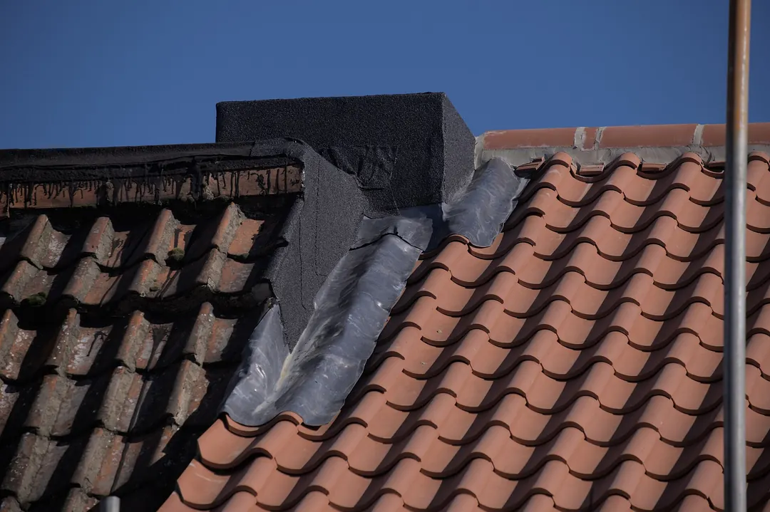 Lead flashing dressed over clay pantiles where the roof meets a brick parapet wall