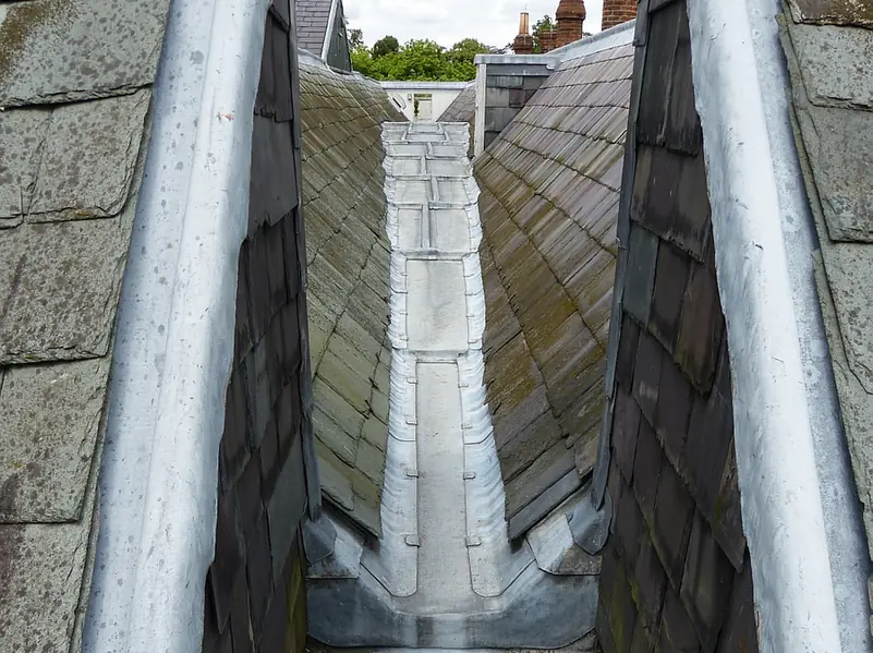 Lead-lined box gutter running between two slate roof slopes, with stepped lead drips and a chimney beyond