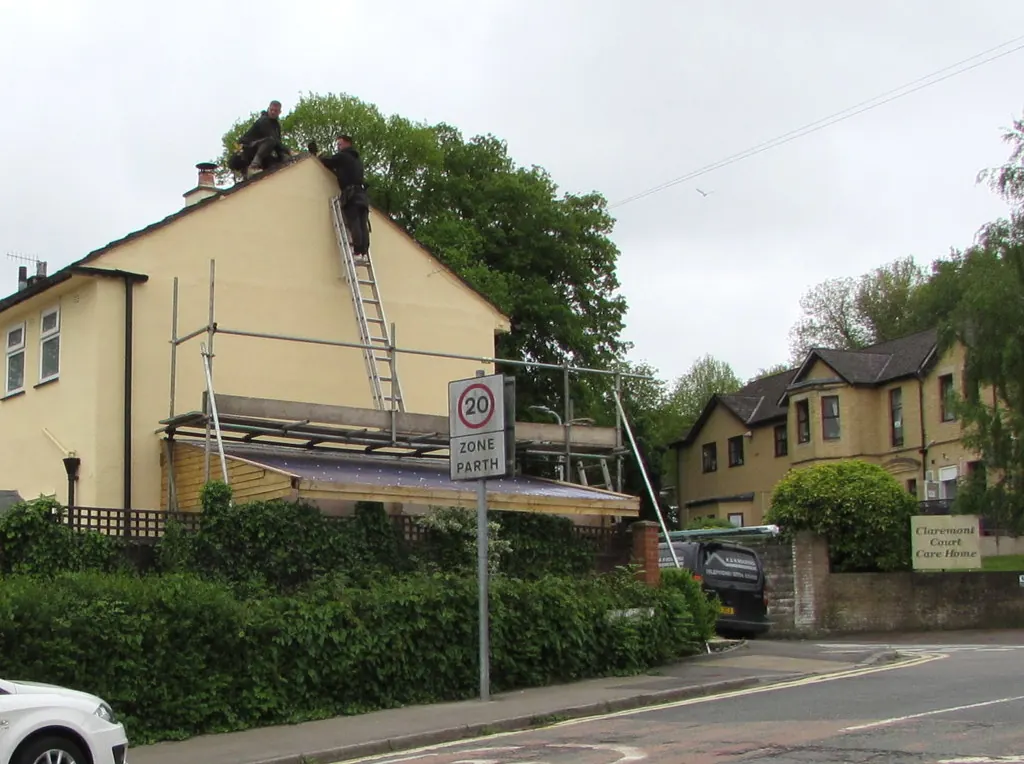 Roofer on a ladder at the gable of a rendered house, with a second worker on the ridge looking over the roof