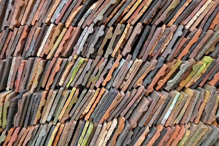 Stack of reclaimed handmade clay peg tiles in mixed reds, browns and greens, set aside for re-use on a re-roof