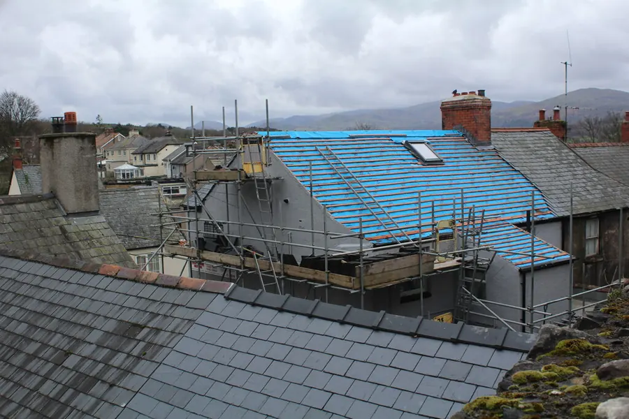 Terraced house mid re-roof with scaffold up and new blue membrane laid over the rafters, slate roofs of neighbouring houses in the foreground
