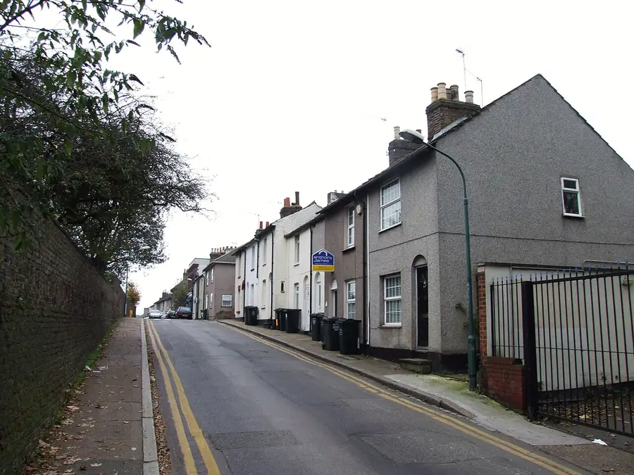 Small rendered terraced houses with chimney stacks climbing Great Queen Street, Dartford