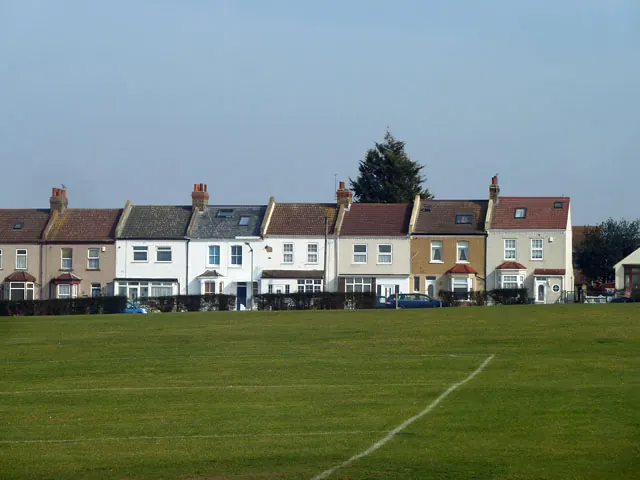 Terraced houses with slate and tiled roofs seen across the green on Acacia Road, Stone