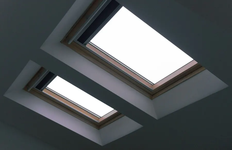 Two roof windows with timber frames set into a sloped plastered loft ceiling, seen from inside